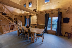 Un intérieur en bois comprenant une table à manger, des chaises, un escalier et une vue par les fenêtres.