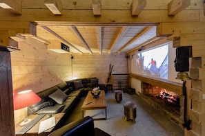 Un salon chaleureux avec une cheminée, des murs en bois, un canapé en cuir et un écran de télévision.