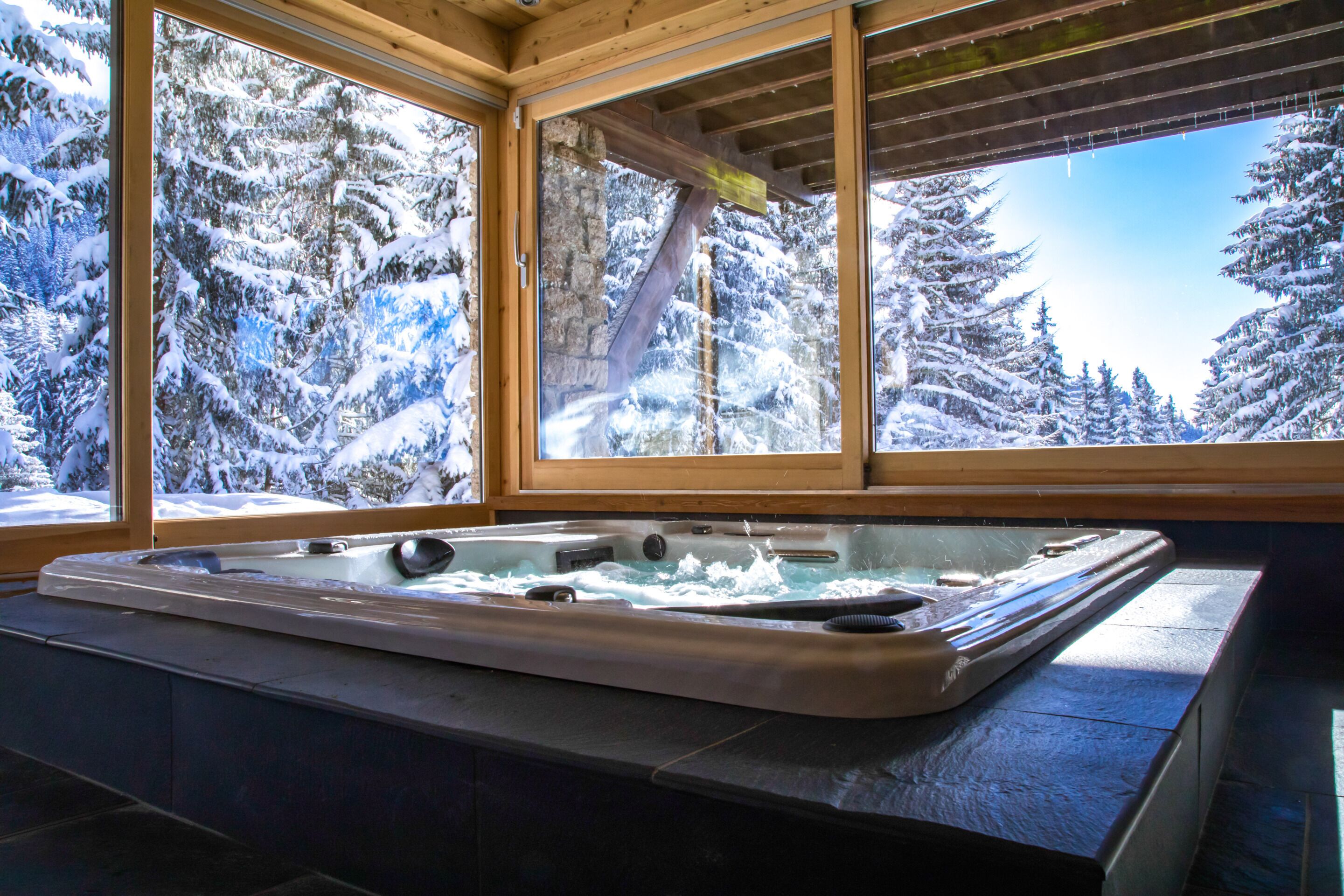 A hot tub in a cabin with large windows overlooking a snowy forest.