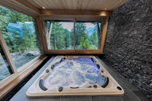 Ein Whirlpool mit Steinwand und Blick auf einen Wald.