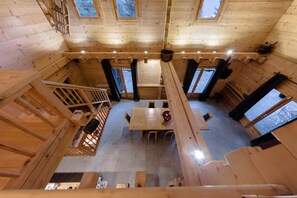Ein Holzblockhaus-Interieur mit einem zentralen Esstisch, mehreren Fenstern und einer Treppe.