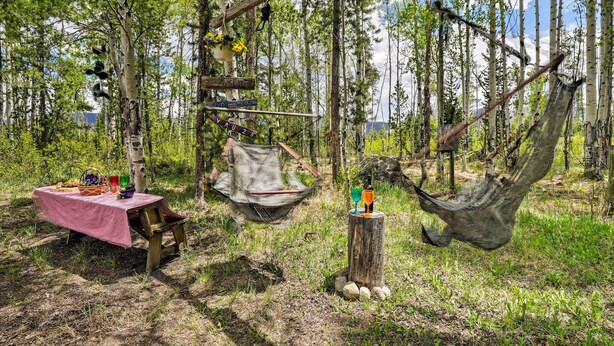 Un entorno rústico al aire libre con una mesa de picnic, una hamaca y un sillón colgante.