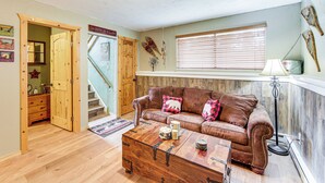 Una sala de estar acogedora con un sofá de cuero marrón, una mesa de centro de madera y una escalera que conduce a otra habitación.
