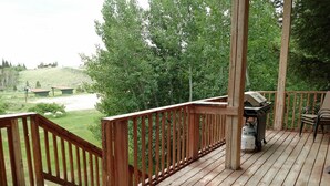 A wooden deck with a railing, a barbecue grill, and a trash can. - Mountain Cabin boasting several outdoor amenities for all seasons (Centennial)
