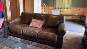 A brown leather sofa with patterned cushions, a wooden cabinet, a wooden bench, and a fire extinguisher. - Mountain Cabin boasting several outdoor amenities for all seasons (Centennial)