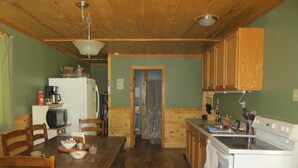 A cozy kitchen with wooden cabinets, a dining table with chairs, a refrigerator, a microwave, and a stove. - Mountain Cabin boasting several outdoor amenities for all seasons (Centennial)