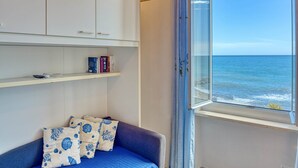 Een kamer met uitzicht op de oceaan, een blauwe bank met gekleurde kussens en witte kasten met boeken.