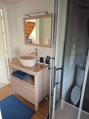 Ein Badezimmer mit einem Holzkosmetikschrank, einem großen Spiegel, einem runden Waschbecken und einer Duschkabine aus Glas.