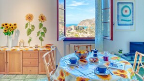 Un'area pranzo con un tavolo apparecchiato per la colazione, vista mare e un quadro appeso al muro.