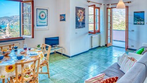 Een lichte woonkamer met een bank, een eettafel met stoelen, een televisie en kunst aan de muren.