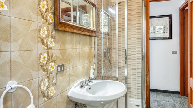 Un bagno con un lavandino bianco, una cabina doccia in vetro e uno specchio con cornice in legno.