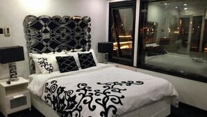 A modern bedroom with a large bed, a decorative headboard, bedside tables, and a large window with a view of the city. - The HouseBoat Mermaid (Dubai)