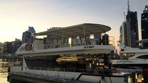 A large yacht docked at a marina with a covered deck area, surrounded by high-rise buildings. - The HouseBoat Mermaid (Dubai)