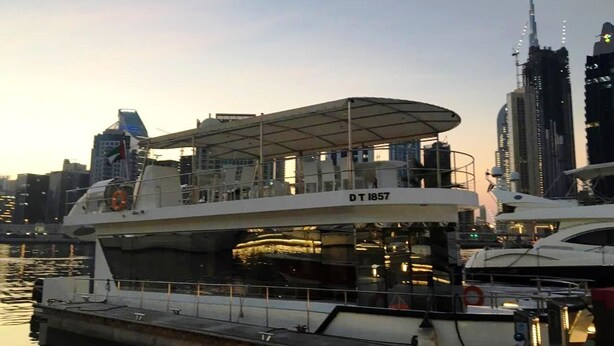 A large yacht docked at a marina with a covered deck area, surrounded by high-rise buildings. - The HouseBoat Mermaid (Dubai)