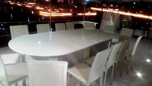 A large oval table with white chairs in a room with a view of a cityscape at night. - The HouseBoat Mermaid (Dubai)