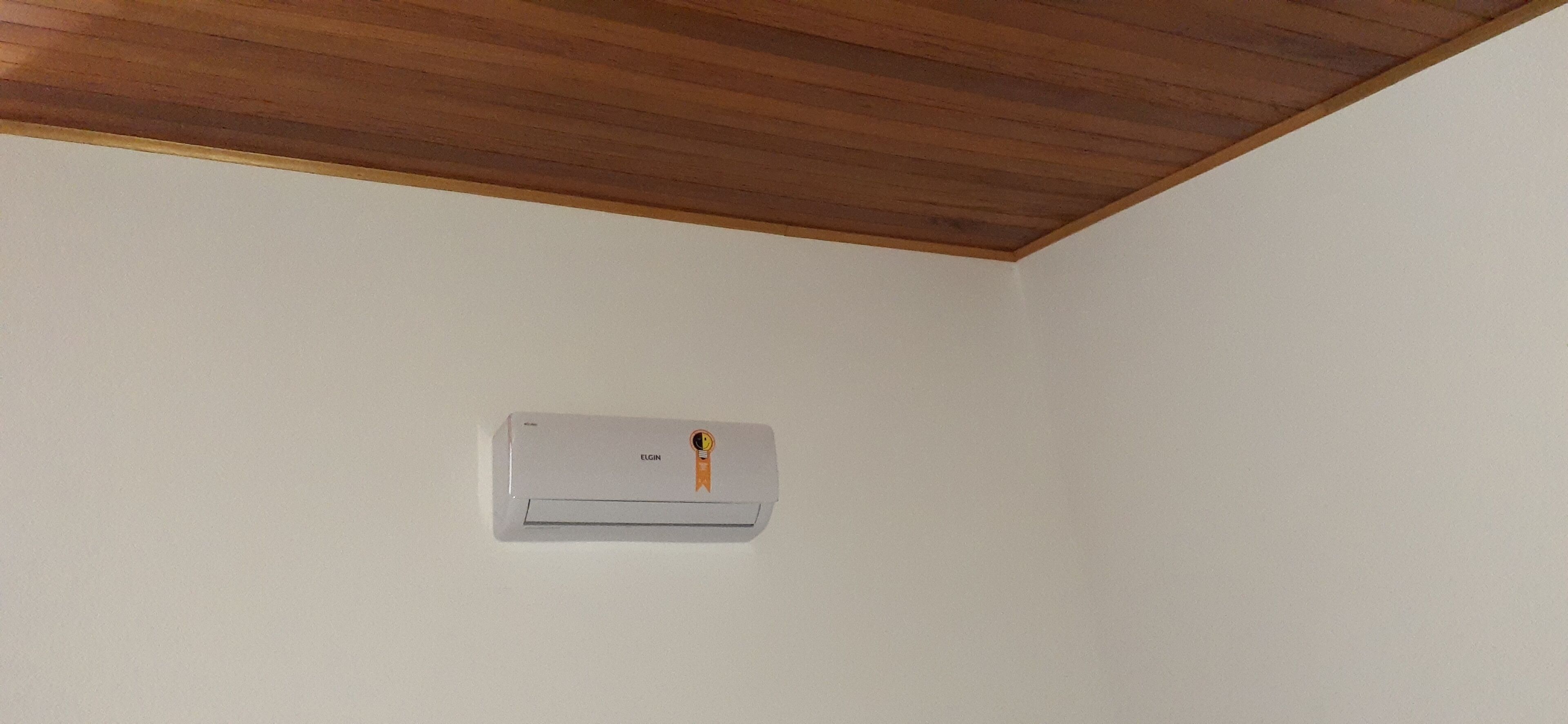 Un equipo de aire acondicionado blanco instalado en una pared lisa con techo de madera.