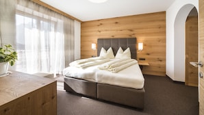A modern hotel room with a large bed, wooden panel walls, a desk, and a potted plant. - Mittendorf Klimaresidence (Schenna)