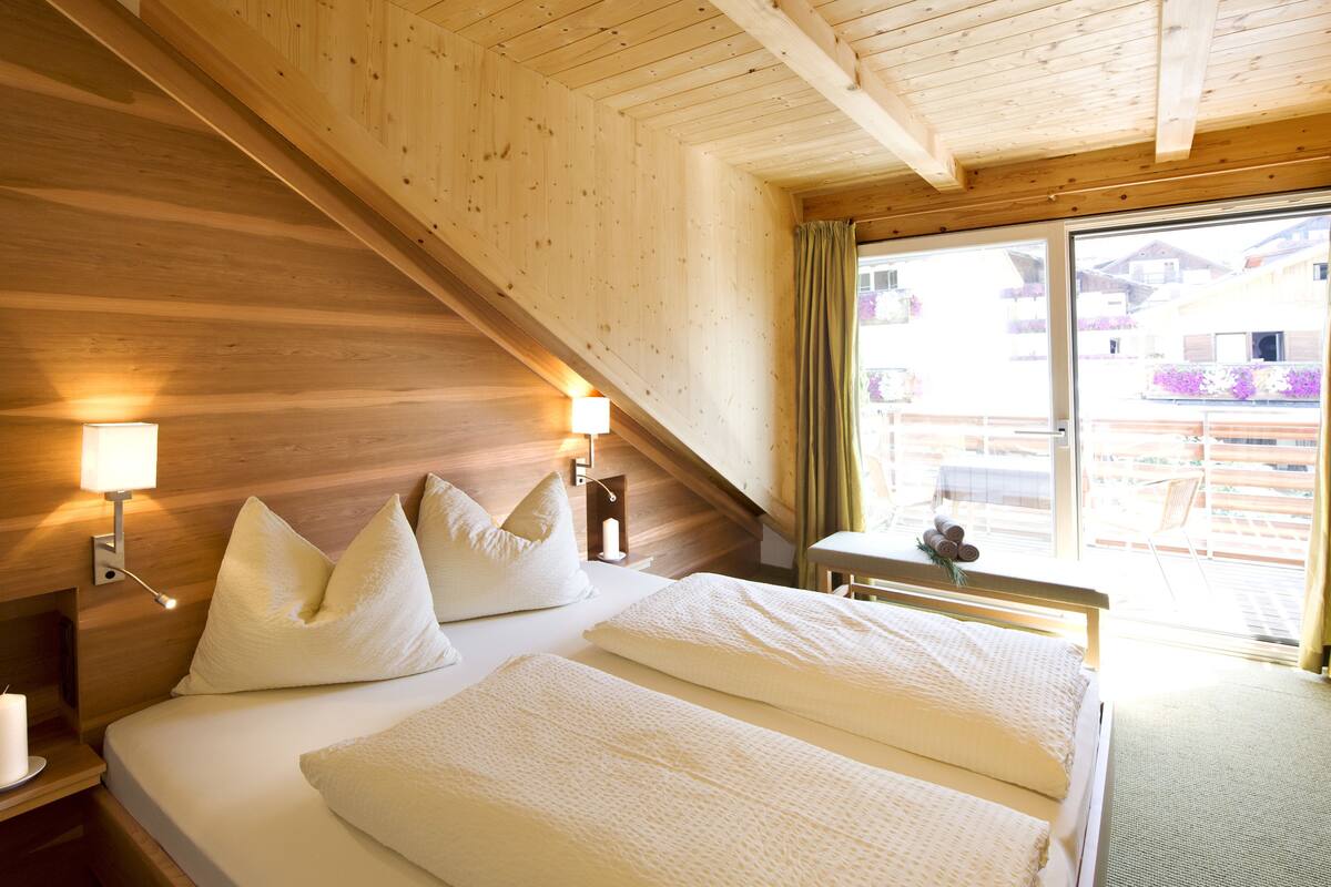 A hotel room with a wooden ceiling, a bed with white bedding, two bedside lamps, and a window with curtains.