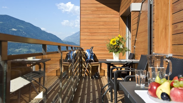 A wooden deck with outdoor seating, a table with fruit, and a view of mountains. - Mittendorf Klimaresidence (Schenna)
