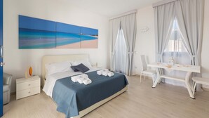 Habitación de hotel con cama, escritorio y silla. Hay un cuadro en la pared y una ventana con cortinas.