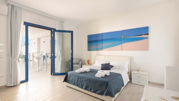 Habitación de hotel con cama, mesita de noche, un cuadro de playa y vista al exterior.