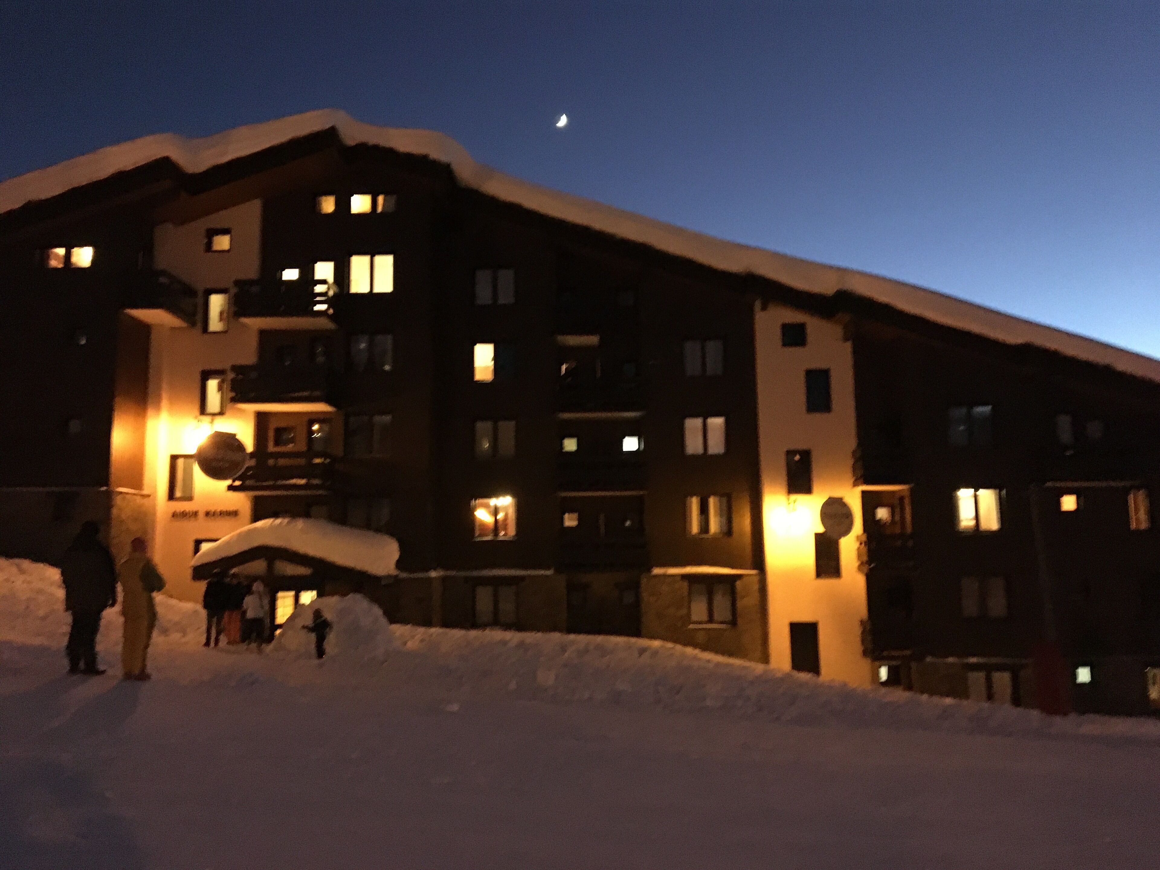 En hög byggnad med flera våningar och upplysta fönster på natten, omgiven av snö.