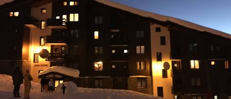 En hög byggnad med flera våningar och upplysta fönster på natten, omgiven av snö.
