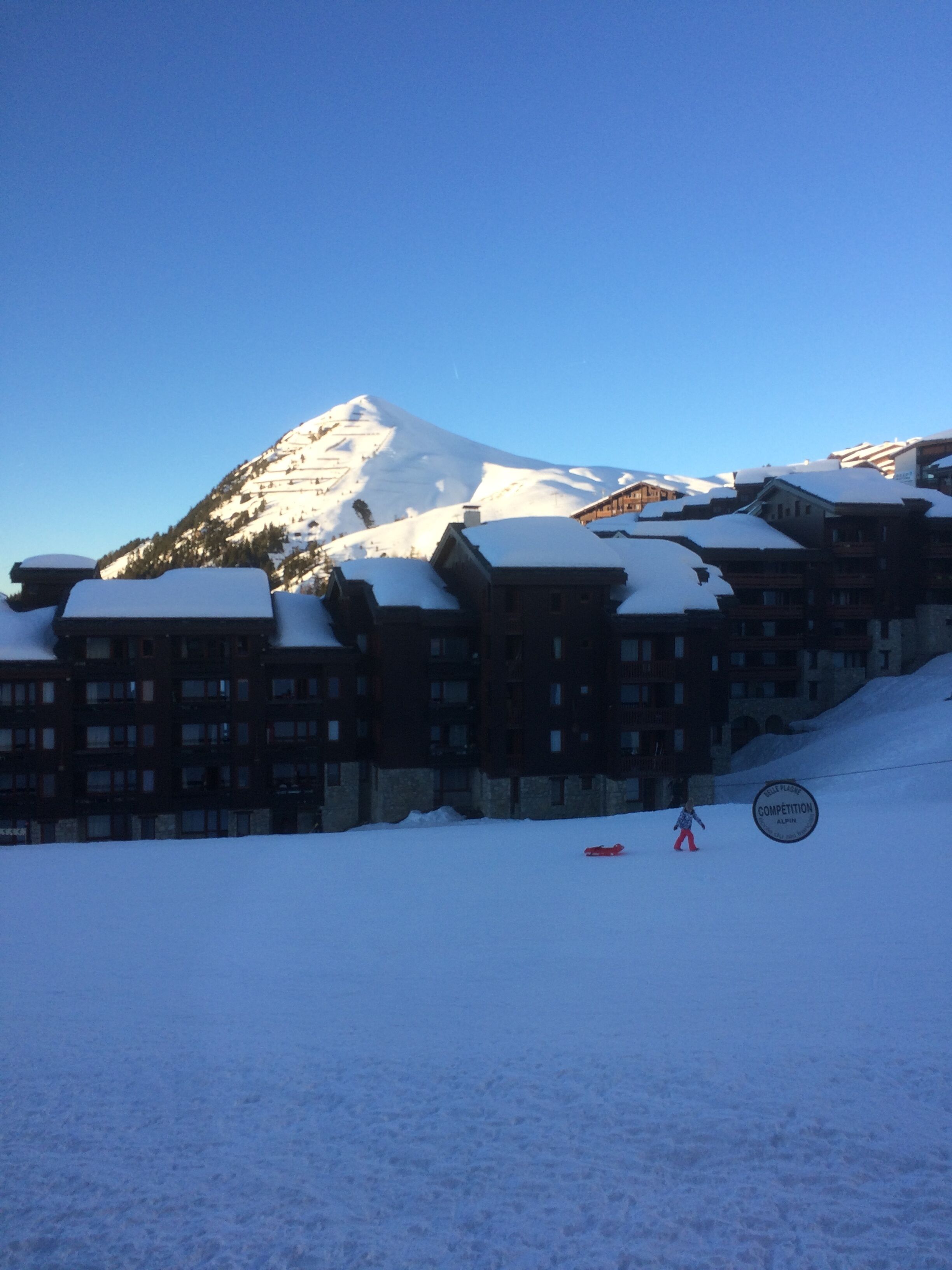 A snow-covered mountain with a ski resort building in the foreground.