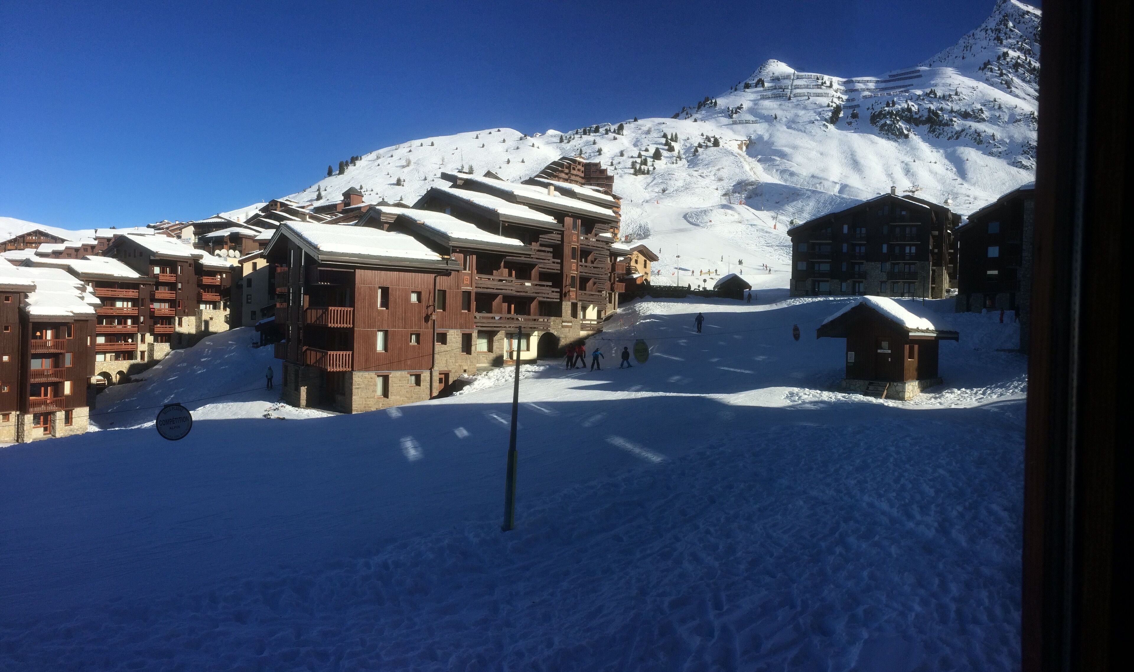Una località montana innevata con edifici in legno, piste da sci e un cielo azzurro limpido.