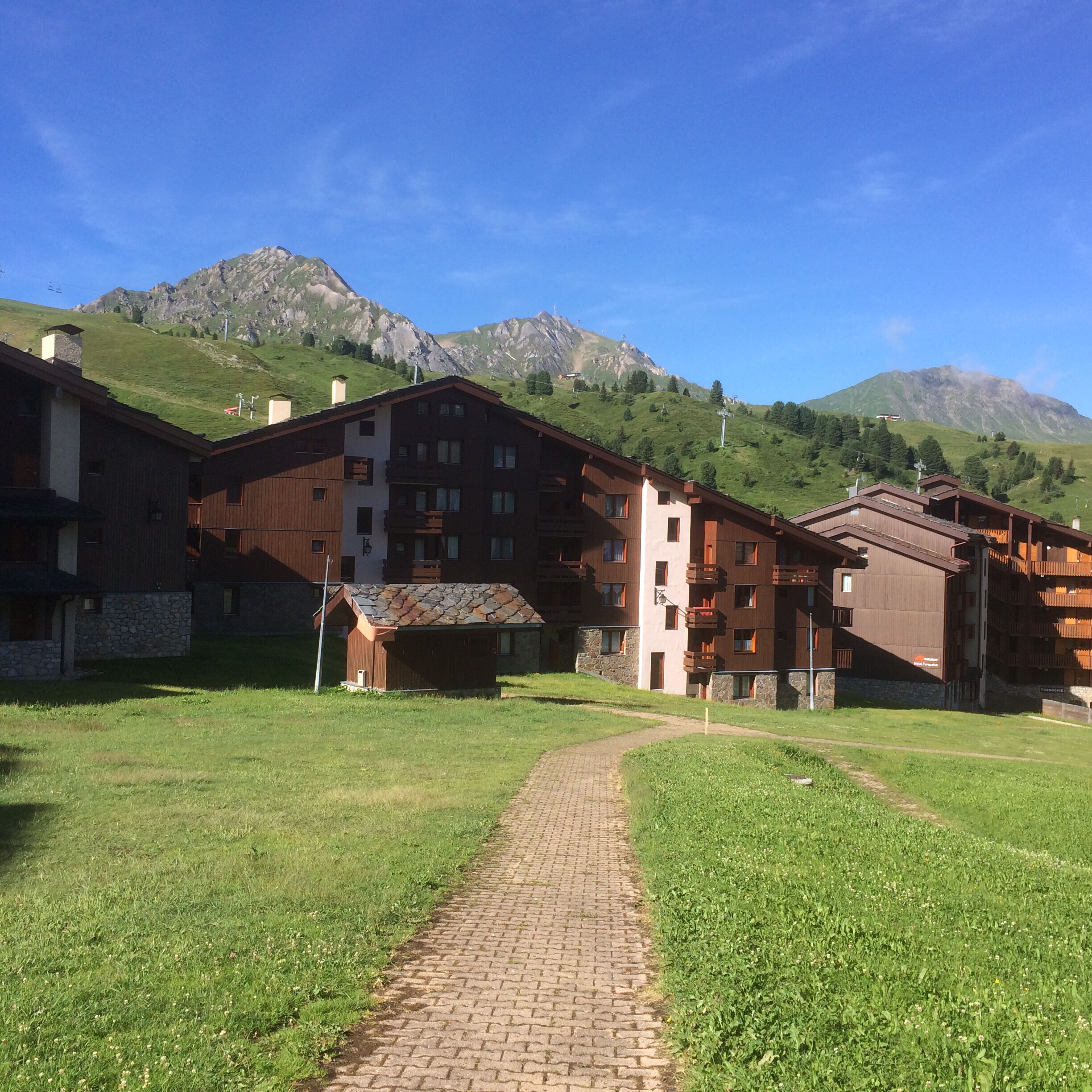 A hotel with a brick pathway leading to a building with multiple balconies and a mountain backdrop.