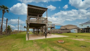 A two-story wooden structure with a balcony, surrounded by a grassy yard and a clear sky.