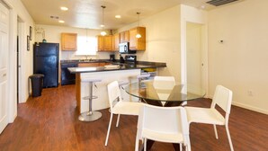 A compact kitchen with wooden cabinets, a black refrigerator, a microwave, and a glass dining table with white chairs.