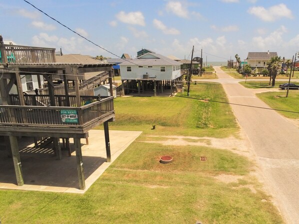 A coastal residential area with a wooden structure labeled for rent, a grassy lawn, and a road leading to the beach.