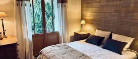 A bedroom with a bed, bedside lamps, a window with curtains, and a wooden wall.
