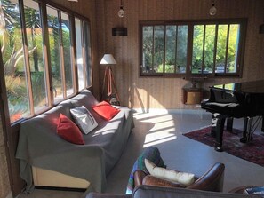 A modern living room with a sofa, armchairs, a piano, and large windows.