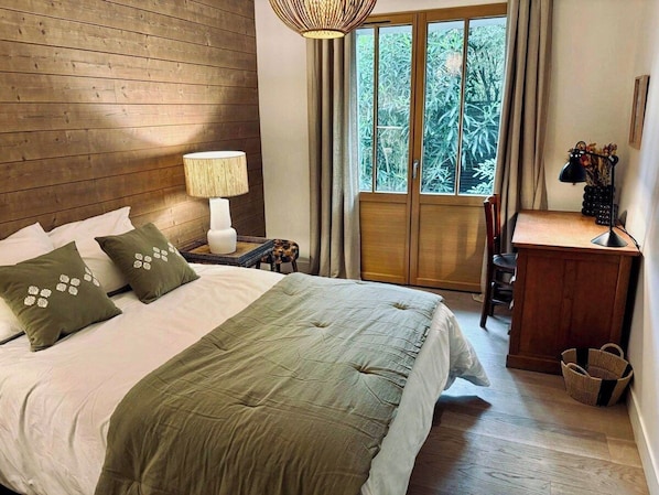 Un dormitorio con cama, escritorio, lámpara y ventana con cortinas.