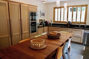 A modern kitchen with wooden cabinets, stainless steel appliances, and a wooden dining table with chairs. - High standard Villa, heated Pool +aircon A0335 (Lège-Cap-Ferret)
