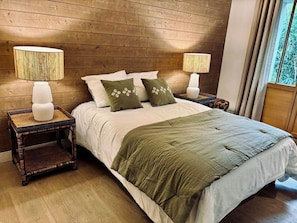 A bed with a green bedspread, two white pillows, and two green decorative pillows. There are two bedside lamps on wooden nightstands.
