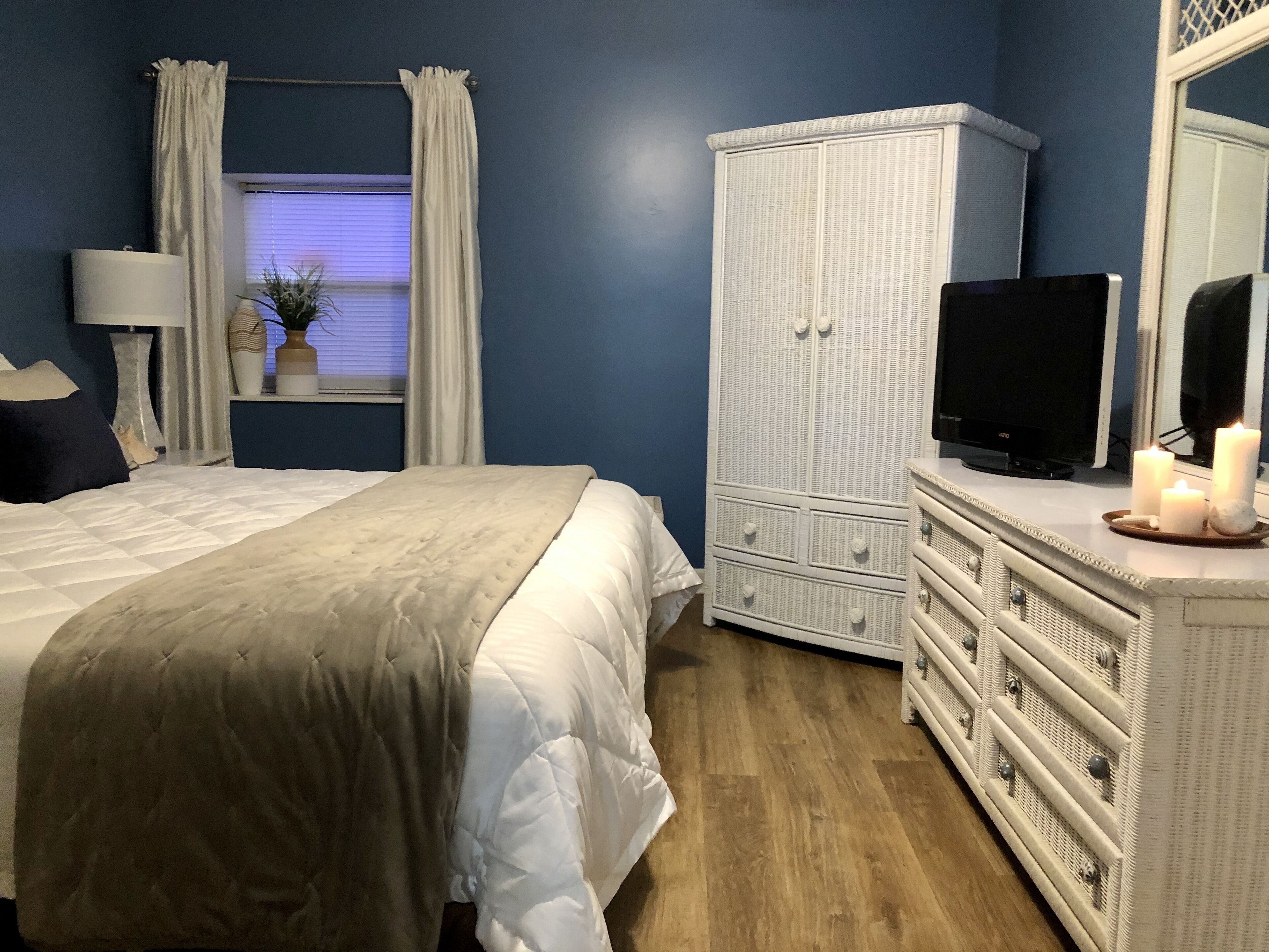 A bedroom with a bed, dresser, TV, and a window with curtains.