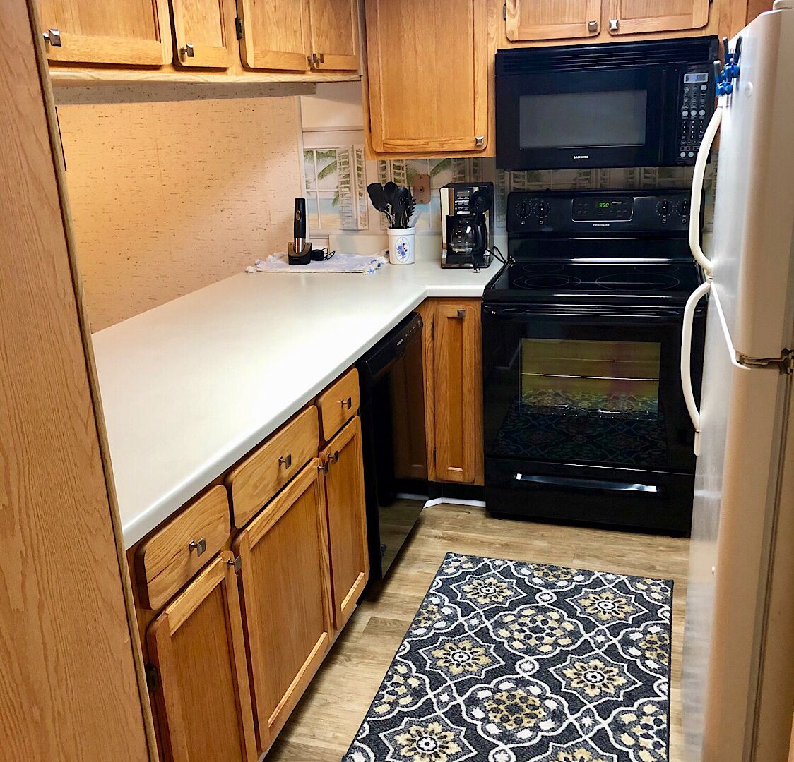 Una cocina compacta con armarios de madera, microondas, estufa y refrigerador.