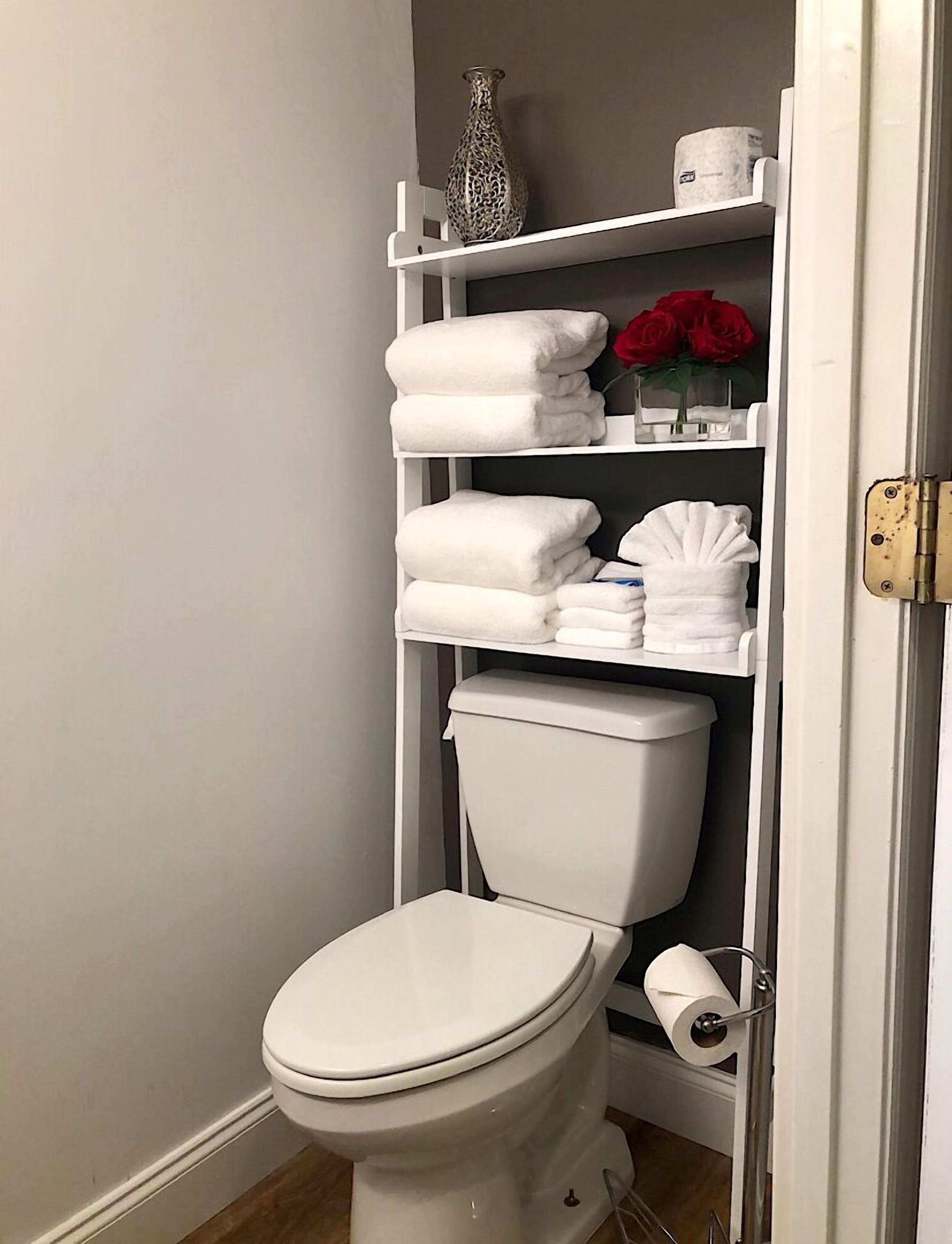 Een kleine badkamer met toilet, een plank met opgevouwen handdoeken, een vaas en een toiletpapierhouder.