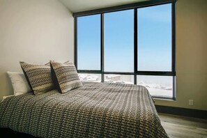 Une chambre avec une grande fenêtre, une couvre-lit à motifs et deux oreillers.