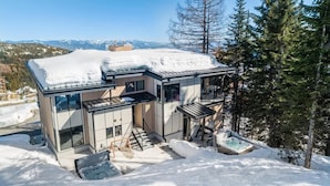 En moderne hytte med to etager, glasfacade, jacuzzi og udsigt til sneklædte bjerge.
