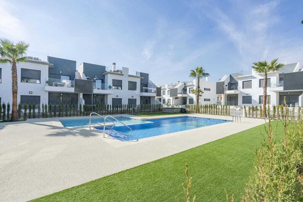 Un complejo residencial moderno con piscina, rodeado de césped cuidado y palmeras.