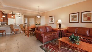 A spacious living room with a brown leather sofa, a dining area with wicker chairs, and a kitchen with wooden cabinets and pendant lighting. - 7 Days / 6 Nights Gateaway (Kissimmee)