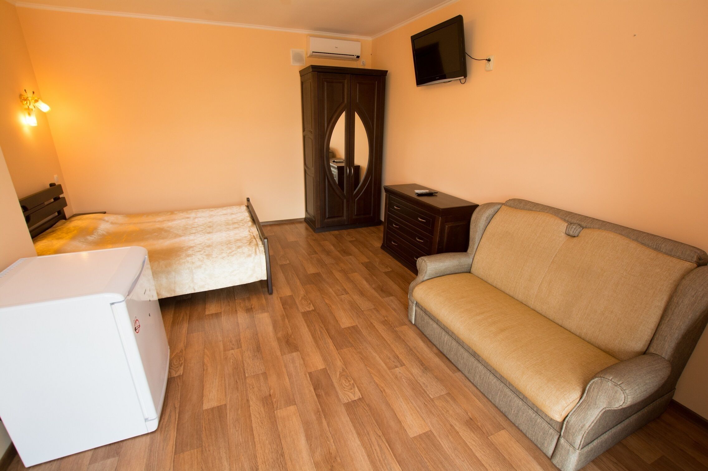 Una habitación con una cama, un sofá, un aparador y un televisor colocado en la pared.