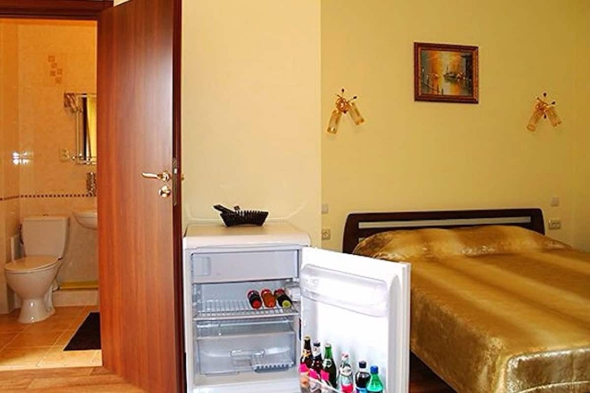 Una habitación de hotel compacta con cama, un refrigerador pequeño, inodoro y zona de ducha.