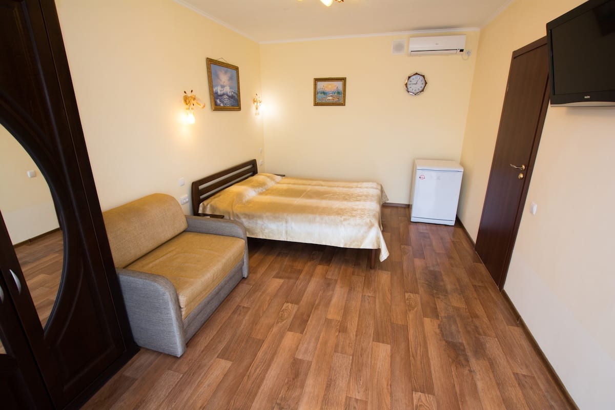 Una habitación con cama, sofá, refrigerador pequeño y televisor.