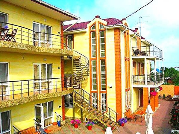 A multi-story residential building with balconies, a staircase, and potted plants.