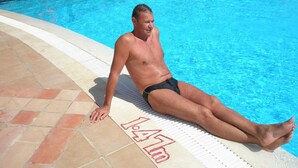 A man sitting by a pool with a diving sign and a lifebuoy in the background. - Adam & Eva (Zatoka)